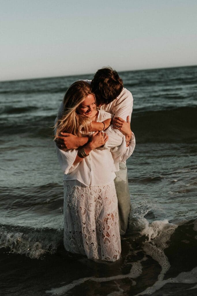guy hugging girl from behind in the sea at beach couple photoshoot