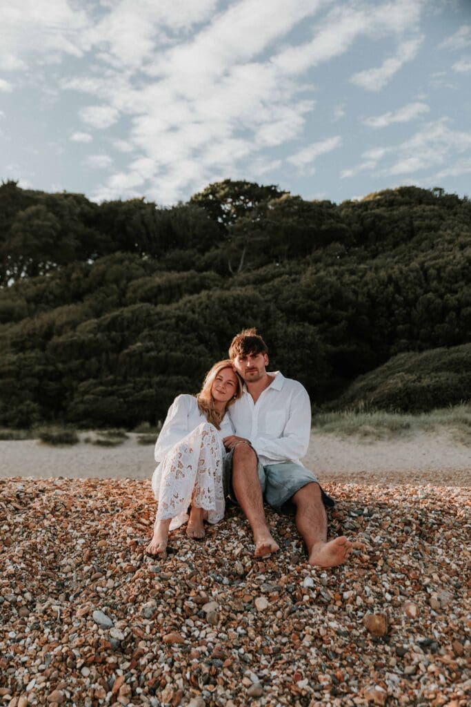 guy and girl leaning on each other sat on pebbles
