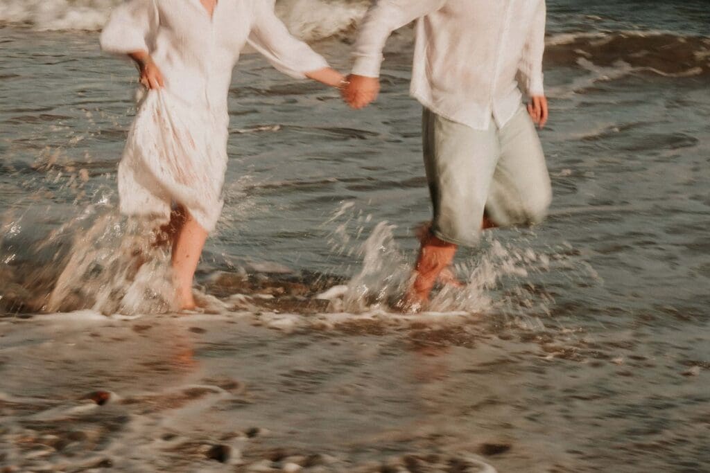 guy and girl running through beach shallows at beach couple photoshoot