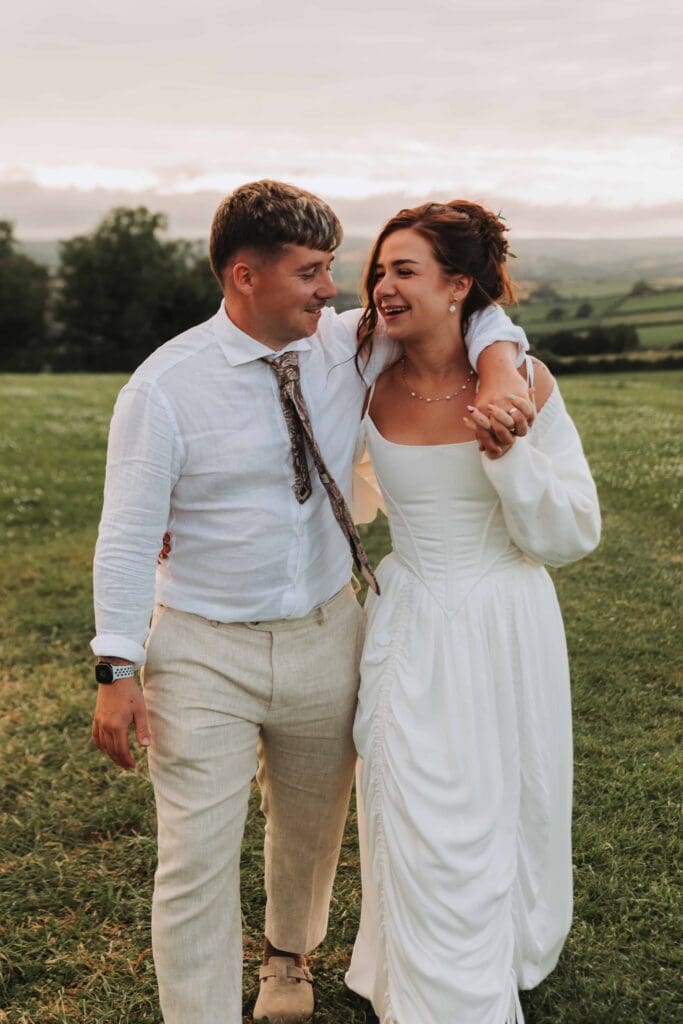 groom with arm round bride walking through field